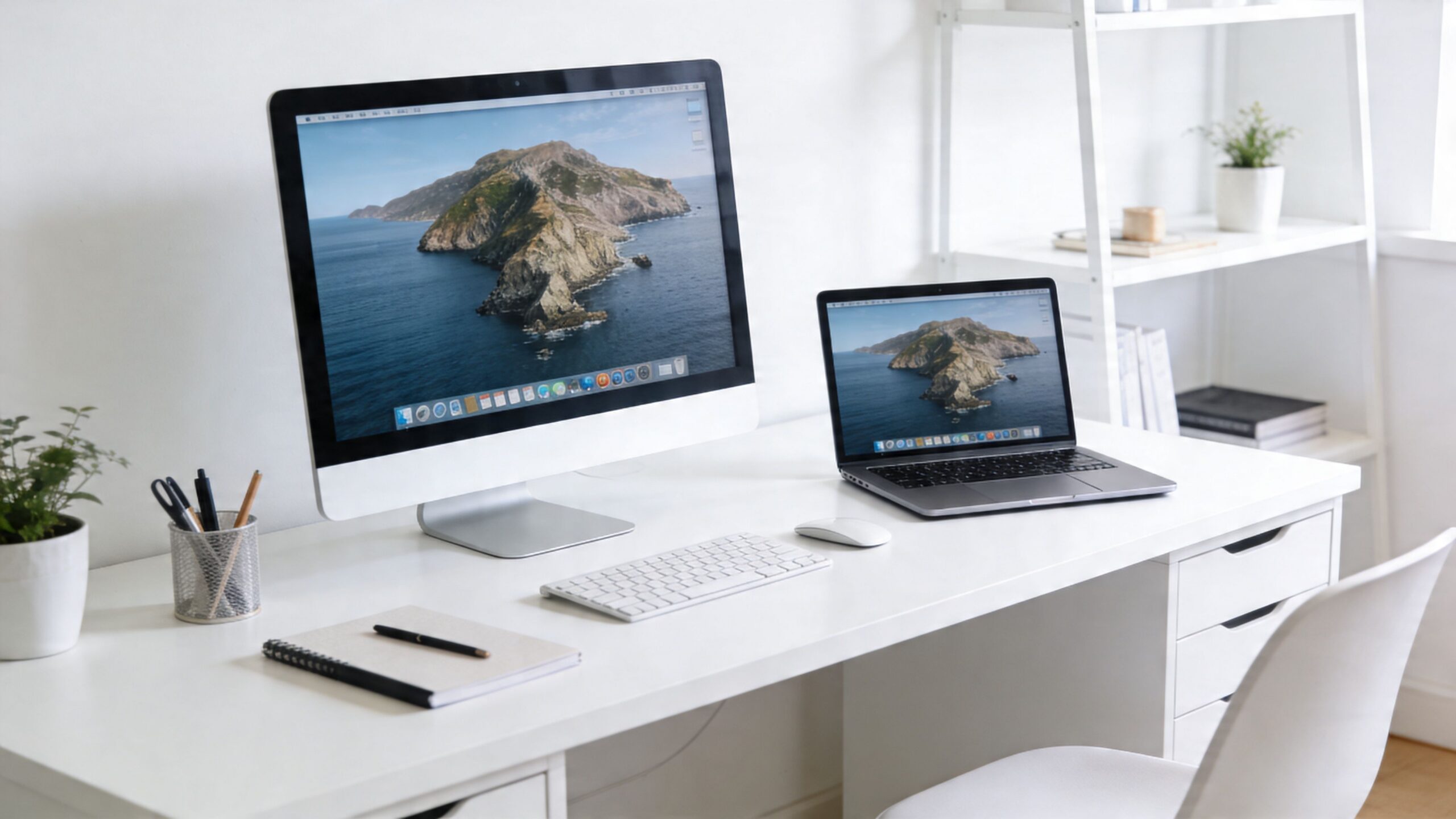 A minimalist white desk setup featuring a desktop computer, laptop, and some stationery in a bright office.